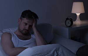 Frustrated man in bed holding head in hands in need of sleep apnea treatment